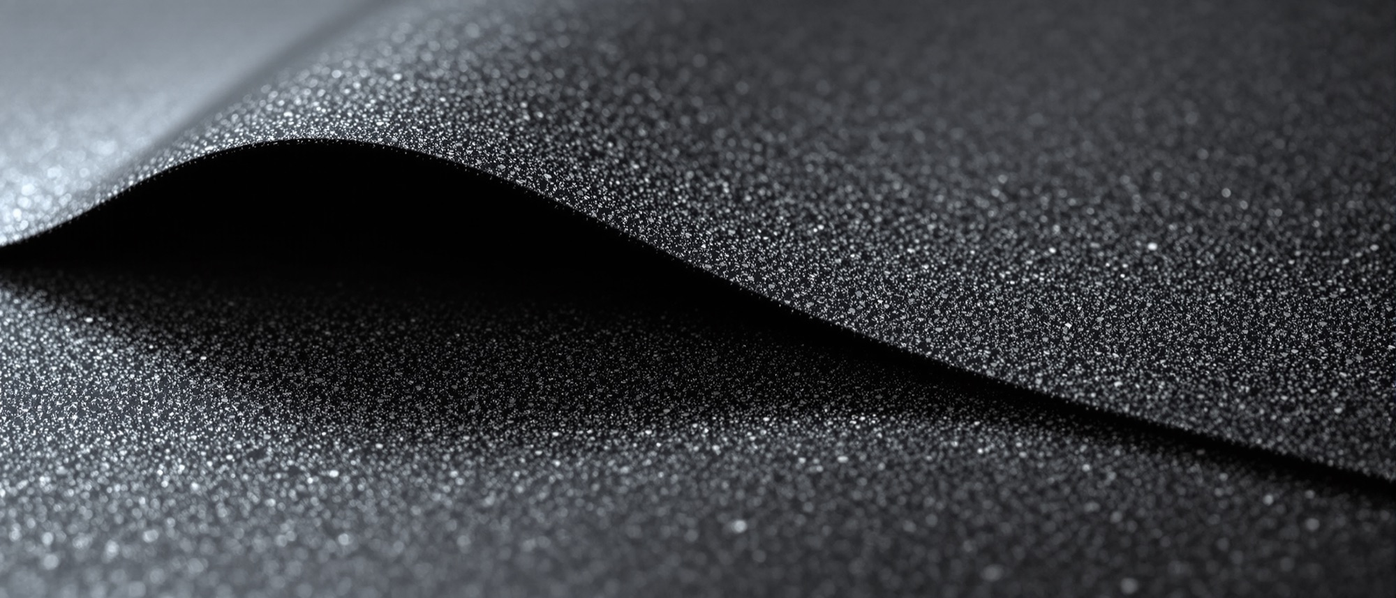 Macro photograph of two sheets of waterproofing membrane overlapping at a lap seam, the upper edge lifted and unbonded with a shadow gap beneath.